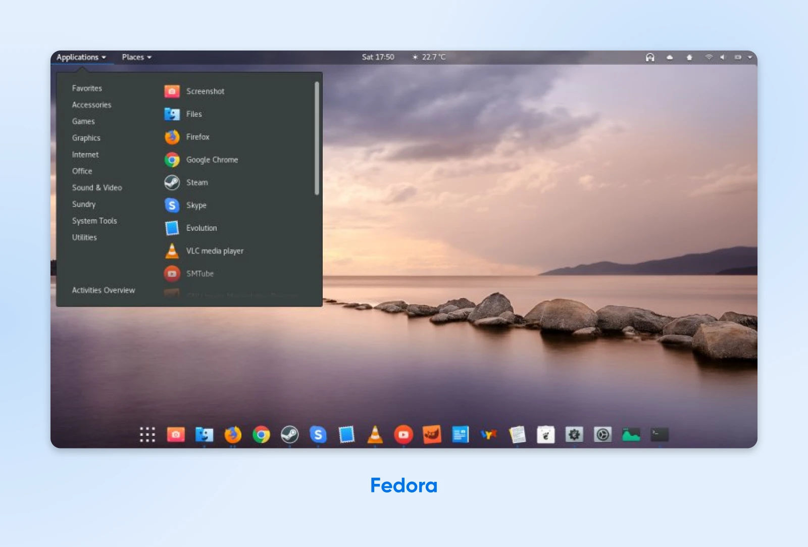 Fedora Linux desktop with a scenic landscape wallpaper showing a lake with rocks in the foreground and mountains.