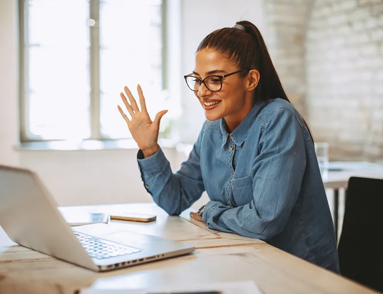 Woman waving to video call on laptop