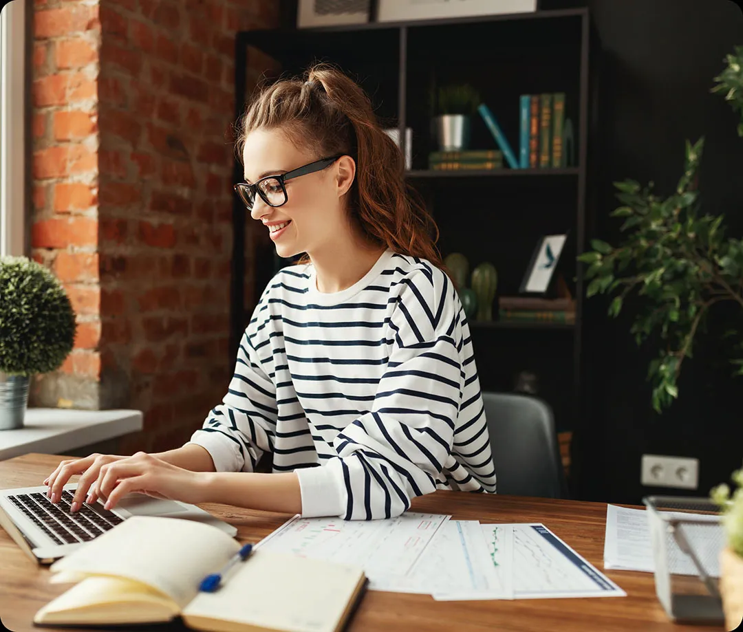 woman sitting at desk happily works on her laptop